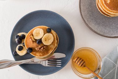 Koyu seramik tabağın üst görüntüsü krep, fındık ve taze muz dilimleri ile tadını artırır. Bir kase bal. Sabah yemeği.