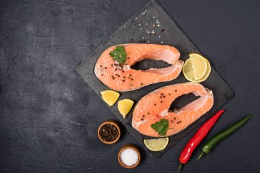 Taş bir tahtada iki çiğ somon bifteği, karabiber, tuz ve limon dilimleri. Omega 3 kaynağı ve doymamış yağlar. Üst Manzara. siyah arkaplan