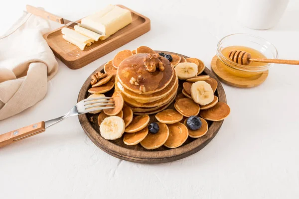 白いテーブルの上の木の板に蜂蜜とナッツとベリーの自家製パンケーキ 健康的な朝食や軽食の概念は ロイヤリティフリーのストック写真