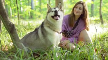 Genç bir kadın ormanda Sibirya köpeğiyle oynuyor.