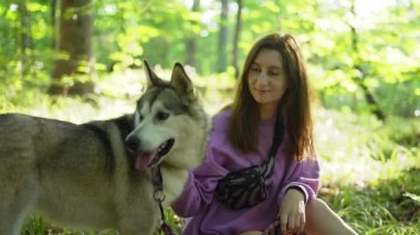 Genç bir kadın ormanda Sibirya köpeğiyle oynuyor.