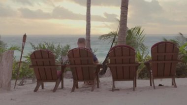 Ortalama 4K 'lık serbest gezgin erkek fotoğrafı. Güzel okyanus kıyısında, gün batımı ve avuçlarında dizüstü bilgisayarıyla çalışıyor.