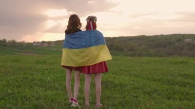 Ukrayna bayrağı taşıyan ve sahada günbatımını izleyen iki kızın geniş açılı 4K görüntüsü. Cesaret ve bağımsızlığın sembolü. Ukrayna 'nın yanında dur