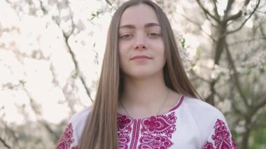Vyshyvanka 'lı güzel Ukraynalı bir kadının 4k pozu - Ukrayna ulusal kıyafetleri. Çiçek açan ağacın yanındaki kırsalda bir kadın..