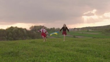 Geleneksel Ukrayna Vysyvanka 'sında elinde Ukrayna bayrağı olan ve gün batımında sahada koşan iki kızın 4K' lık geniş açıyla çekimi. Cesaret ve bağımsızlığın sembolü. Ukrayna 'nın yanında dur