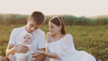 4k slow motion shot - Young family of three - mother, father and daughter having picnic outdoors during beautiful sunset. Slow living and happy family concept