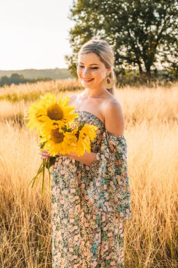 Gün batımında kırsalda mutlu ve hamile bir kadının portresi.