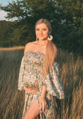 Gün batımında kırsalda mutlu ve hamile bir kadının portresi.