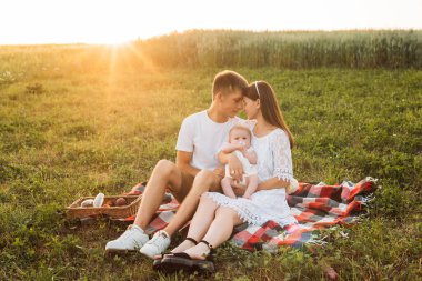 Üç kişilik genç bir aile. Anne, baba ve kız gün batımında dışarıda piknik yapıyorlar. Yavaş yaşam ve mutlu aile kavramı