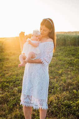 Anne ve kızı tarlada poz veriyor. Küçük bebekle oynamak ve eğlenmek. Mutlu aile kavramı 