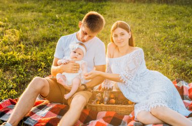 Üç kişilik genç bir aile. Anne, baba ve kız gün batımında dışarıda piknik yapıyorlar. Yavaş yaşam ve mutlu aile kavramı