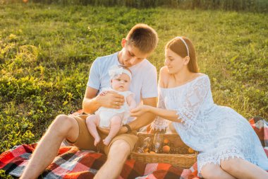 Üç kişilik genç bir aile. Anne, baba ve kız gün batımında dışarıda piknik yapıyorlar. Yavaş yaşam ve mutlu aile kavramı