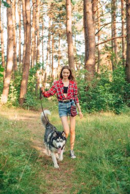 Genç kız Sibirya köpeğiyle oynuyor ve eğleniyor. Ormanda köpekli bir kız