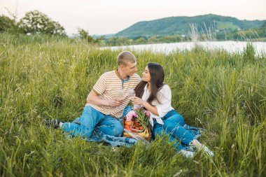 Genç mutlu çift güzel günbatımında kırsal alanda piknik yapıyor. Gölün yanında romantik bir buluşma.