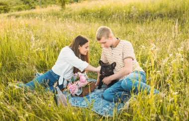 Genç mutlu çift, güzel günbatımında kırsal alanda Fransız buldoglarıyla piknik yapıyor. Gölün yanında romantik bir buluşma.