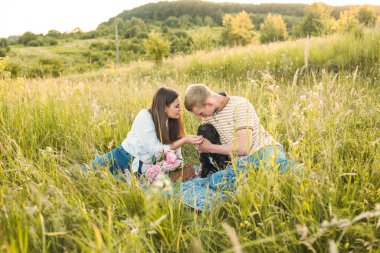 Genç mutlu çift, güzel günbatımında kırsal alanda Fransız buldoglarıyla piknik yapıyor. Gölün yanında romantik bir buluşma.
