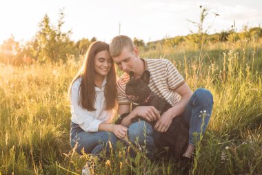 Genç mutlu çift, güzel günbatımında kırsal alanda Fransız buldoglarıyla piknik yapıyor. Gölün yanında romantik bir buluşma.