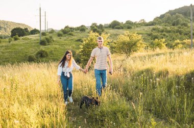 Genç mutlu çift, güzel günbatımında kırsal alanda buldoglarıyla eğleniyor.