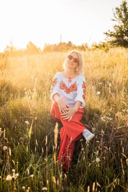 Mutlu, neşeli, olgun bir kadının güzel günbatımında taşrada portresi.