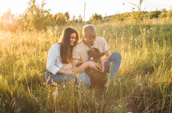 Genç mutlu çift, güzel günbatımında kırsal alanda Fransız buldoglarıyla piknik yapıyor. Gölün yanında romantik bir buluşma.