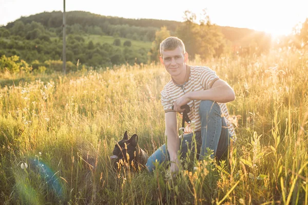 Genç ve mutlu bir adam güzel gün batımında kırsalda Fransız buldoguyla dinleniyor.