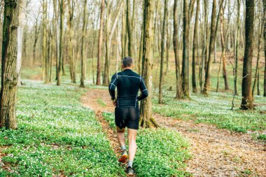 Güzel bahar ormanlarında koşan sporcu adamın geniş açılı görüntüsü. Spor ve sağlık konsepti