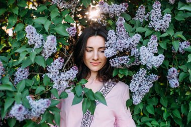 Çiçek açan leylak ağacının yanında vyshyvanka giyen genç ve güzel bir kadın. Ukrayna ulusal kıyafetleri..