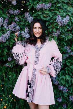 Çiçek açan leylak ağacının yanında vyshyvanka giyen genç ve güzel bir kadın. Ukrayna ulusal kıyafetleri..