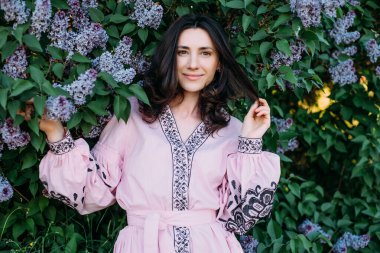 Çiçek açan leylak ağacının yanında vyshyvanka giyen genç ve güzel bir kadın. Ukrayna ulusal kıyafetleri..