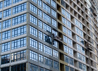 Çok katlı bir binanın inşaatı. Sahne işi. İnşaatçılar pencereleri monte ediyor. İnşaat alanı.