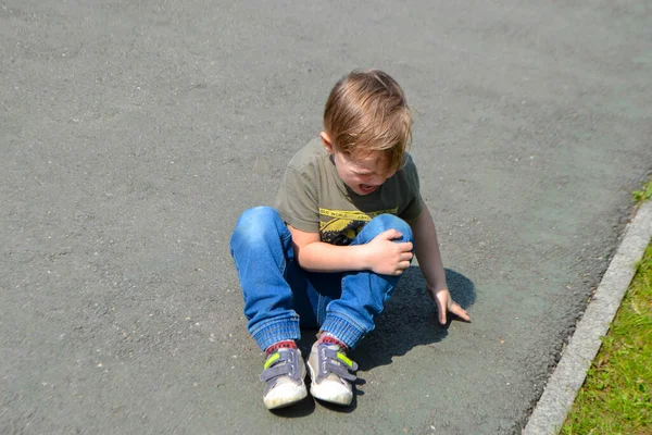 Ein weinender Junge liegt vor Schmerzen auf dem Boden und hält sein Knie — Stockfoto