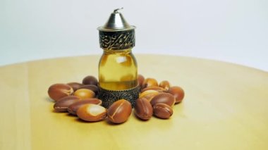 Doğulu cam ve metal bir şişede Argan yağı ve tahta masa ve beyaz arka planda argan fındığı hareketi.
