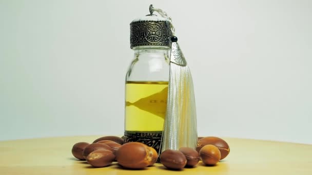 在东方玻璃和金属瓶中的Argan油和在木制桌子和白色背景上运动的argan坚果. — 图库视频影像