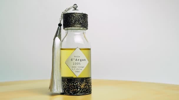 Арганова олія в східному склі і рух металевої пляшки на дерев'яному столі і білому фоні.. — стокове відео