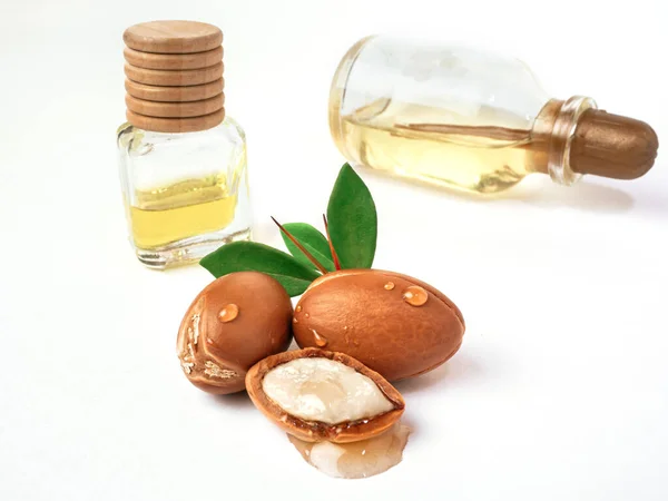 Yeşil yapraklı üç argan fındığı izole edilmiş beyaz arka planda cam şişeler. Bir damla yağla doğranmış argan fındığı. Petrol üretimi için tam ve yarım Fas Argania Spinosa tohumları