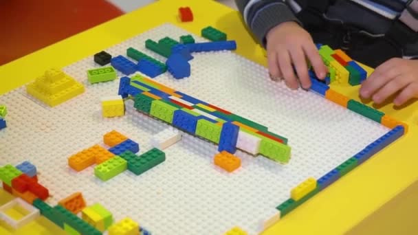 Il bambino raccoglie sulla piattaforma varie strutture con l'aiuto di un costruttore di blocchi. Ragazzo prescolare raccoglie una figura con un modello utilizzando chip colorati in giardino. — Video Stock