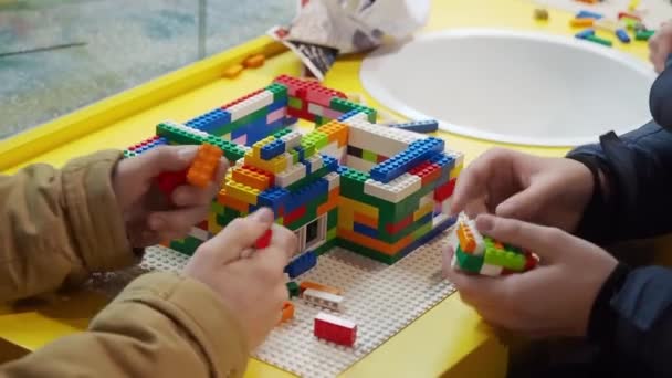 Dzieci zbierają na platformie różne konstrukcje przy pomocy konstruktora bloków. Dwóch chłopców zbiera figurę z wzorem za pomocą kolorowych żetonów na placu zabaw zbliżenie — Wideo stockowe