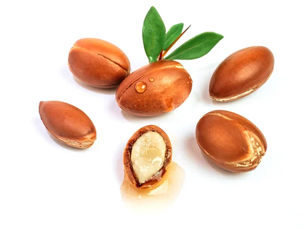 Frutti di Argan con foglie verdi su fondo bianco isolato. Nocciola di argan tritata con una goccia d'olio. Semi di Argania Spinosa interi e mezzo marocchini per la produzione di olio — Foto Stock