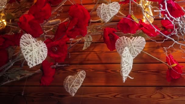 Bildschirmschoner zum Valentinstag. Weiße herzförmige Dekorationen hängen an einer Baumschaukel und drehen sich windgepeitscht vor dem Hintergrund beleuchteter Lichter und trockener Zweige mit Blumen — Stockvideo