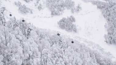 Dağ kışı manzaralı kablo araba hareketi. Dağların, ormanın, yamacın üzerinden. Kayak merkezi. Karda ağaçlar.