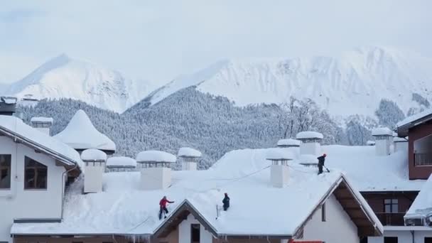 Mensen verwijderen de sneeuw van het dak van de huizen. Brigade van arbeiders scheppen sneeuw van daken na sneeuwstorm in de bergen — Stockvideo