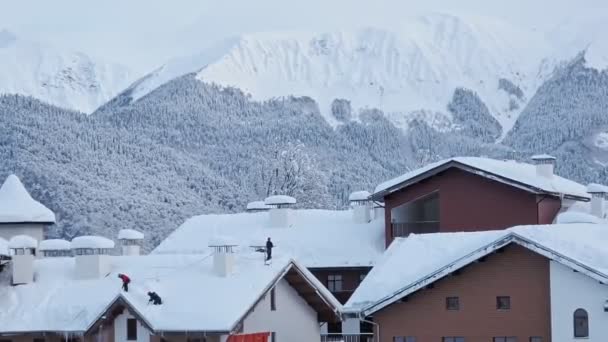 Folk tar bort snön från taket på husen. Brigad av arbetare skyfflar snö från tak efter snöstorm i bergen — Stockvideo