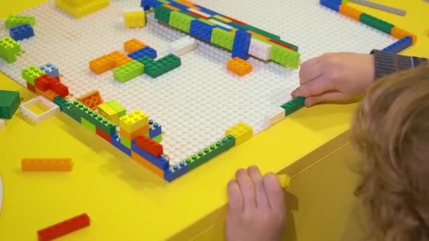 Het kind verzamelt op het platform verschillende structuren met behulp van een blokbouwer. Kleuterschooljongen verzamelt een figuur met een patroon met behulp van gekleurde chips in de tuin. — Stockvideo