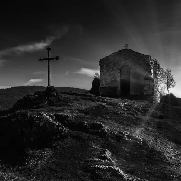 Küçük bir ortaçağ Ortodoks kilisesinin siyah beyaz fotoğrafı ve kayalık bir tepenin üstünde çapraz. Güneş ışınları arka plan