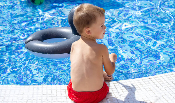 Счастливый ребенок в бассейне играет с водяным пистолетом. Отдых