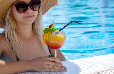 Genç bayan havuzda dinleniyor. Taze sıkılmış portakallı kokteyl içiyor. Rekreasyon