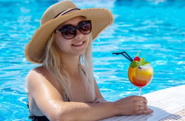 Genç bayan havuzda dinleniyor. Taze sıkılmış portakallı kokteyl içiyor. Rekreasyon