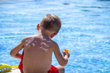Anne oğlunun sırtına krem sürüyor. Bebek cilt bakımı. Seyahat eden güneş kremi. seçici odak