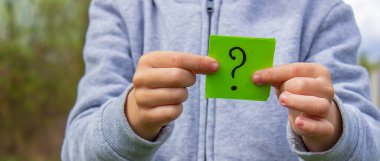 Çocuğun elinde parkın arka planında soru işareti olan çıkartmalar var. Doğa. seçici odak