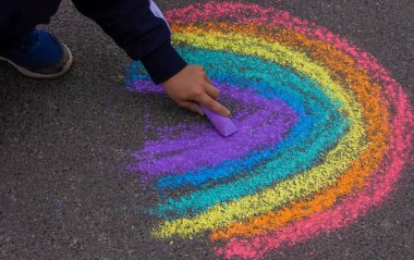 Bir çocuk asfalta bir gökkuşağı çizer. Seçici odaklanma. çocuk.